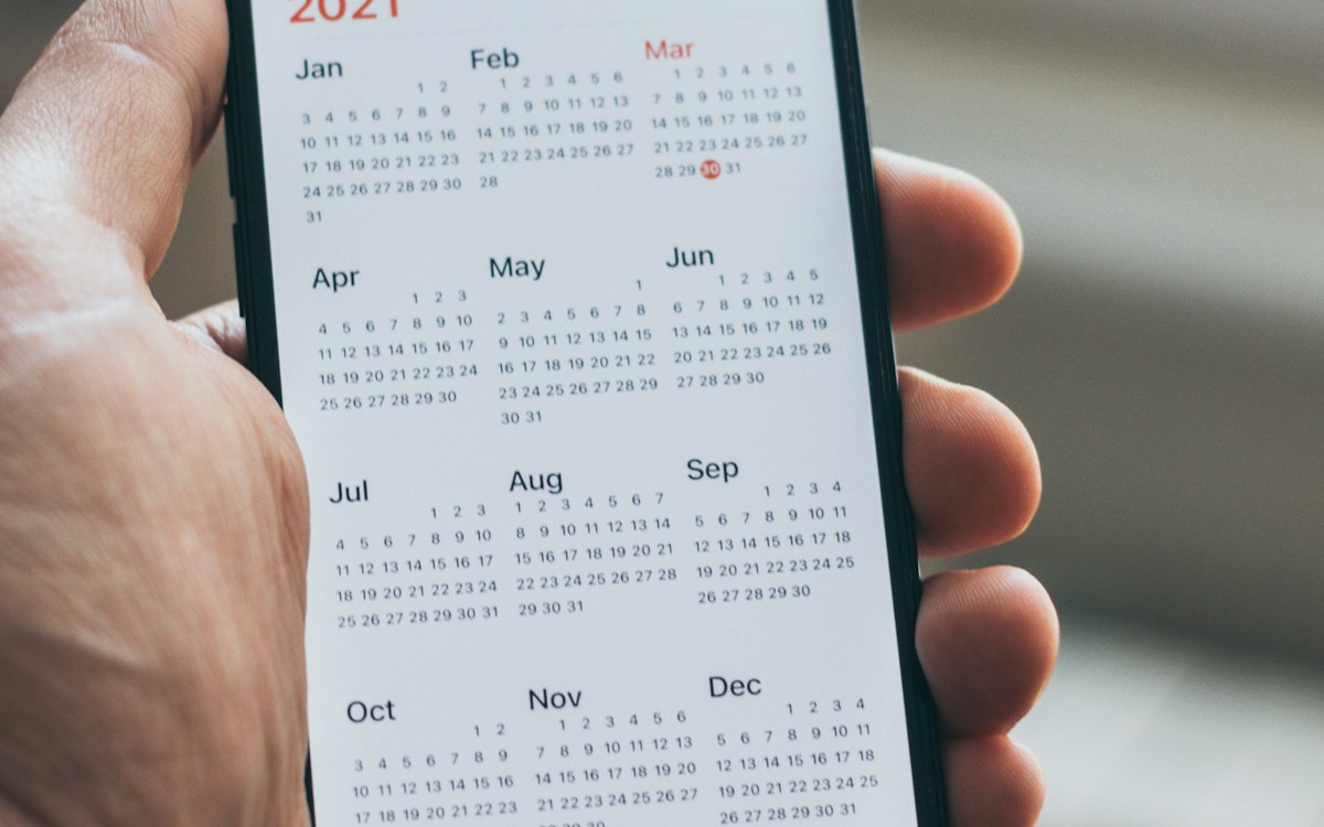 A hand holding a phone that shows a monthly calendar