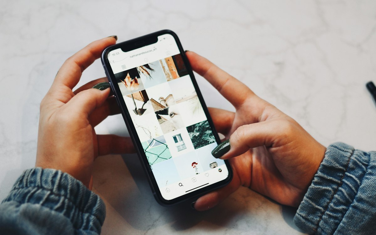 Two hands holding a phone that shows a grid of photos
